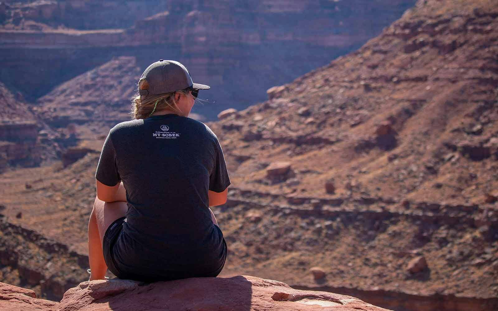 A woman sits on a rock overlooking a canyon.