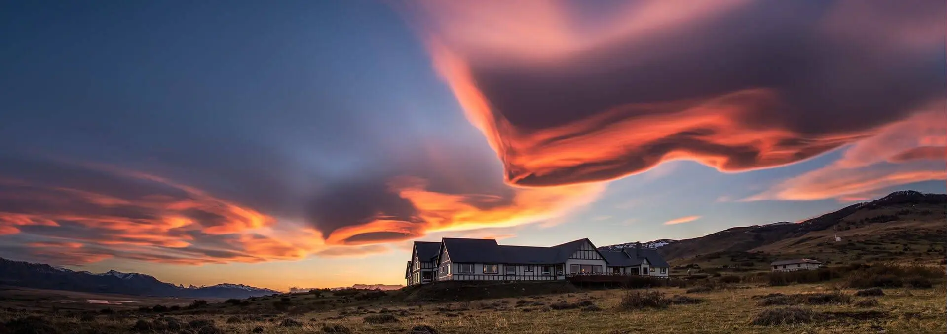 EOLO sits on a grassy plain under a dramatic sky with red and orange cloud formations during sunset. In the background, rolling hills and mountains promise back-to-back adventures for the intrepid explorer.