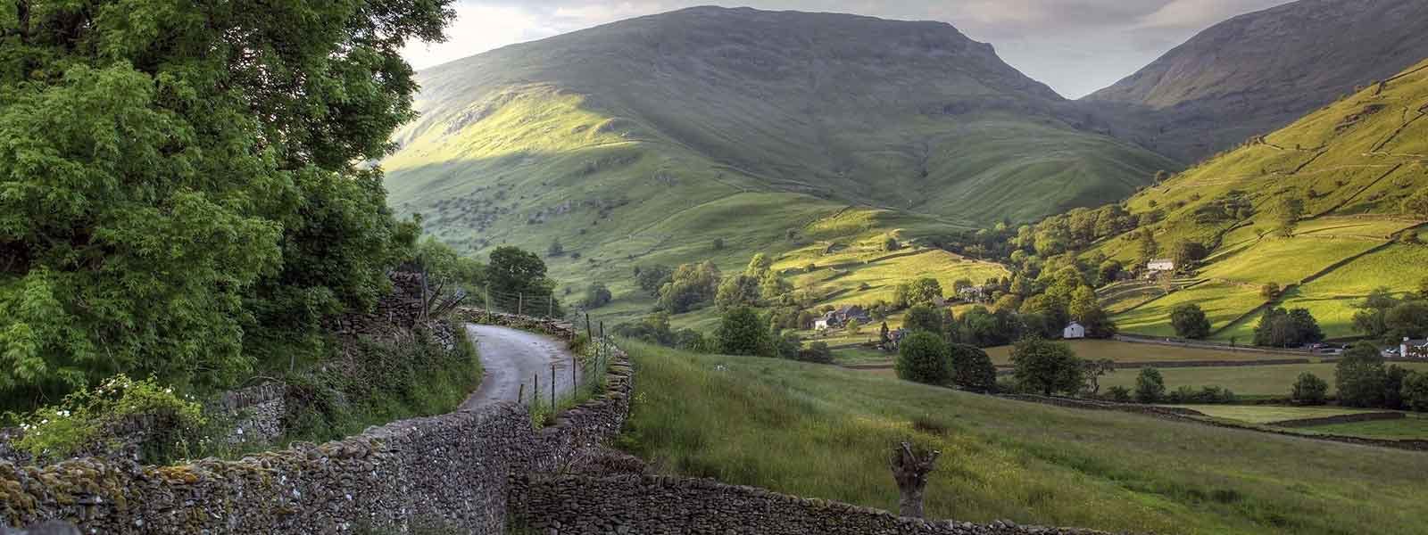 A stone walled road leads to a stunning valley in the mountains on an England walking tour.