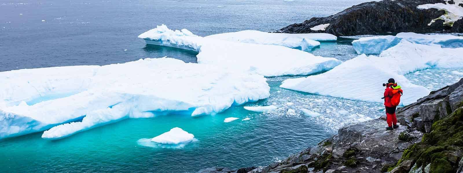 A man is standing on a cliff overlooking icebergs during a polar cruise.