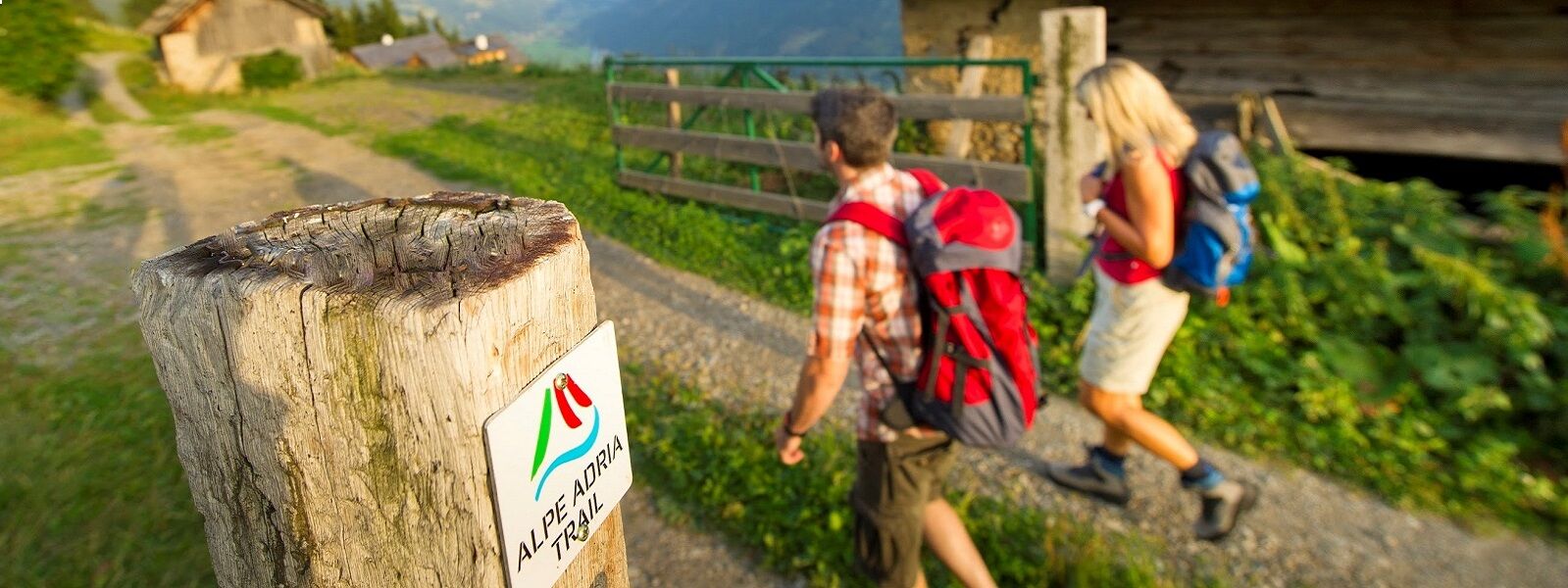 Two people on a multi-country adventure walking down a path with a sign on it.