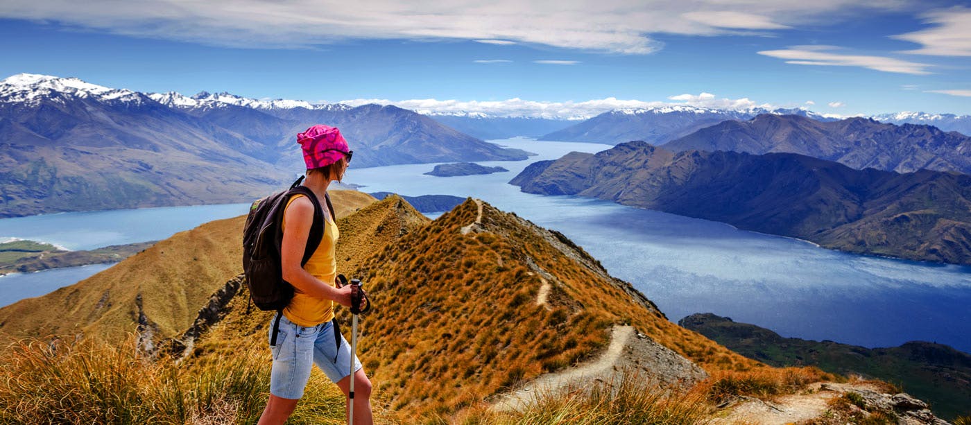 A man is standing on top of a mountain overlooking lake wanaka.