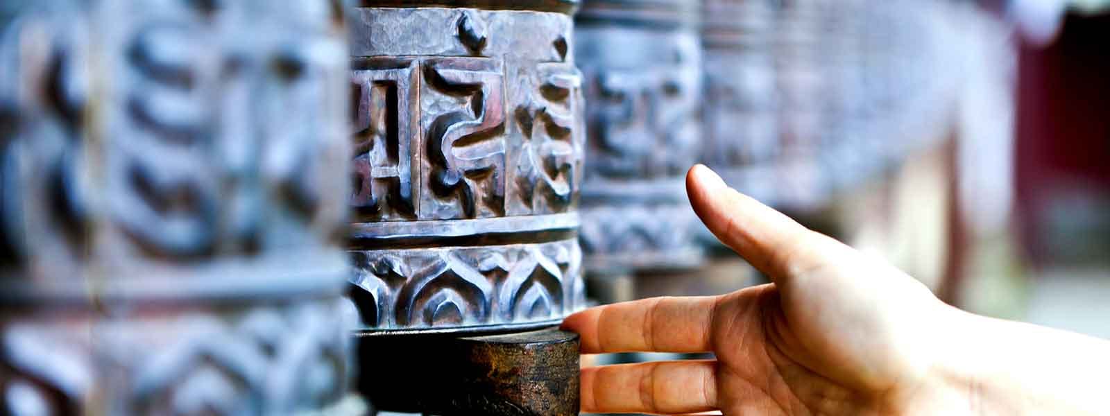 A person's hand reaching for a prayer wheel.