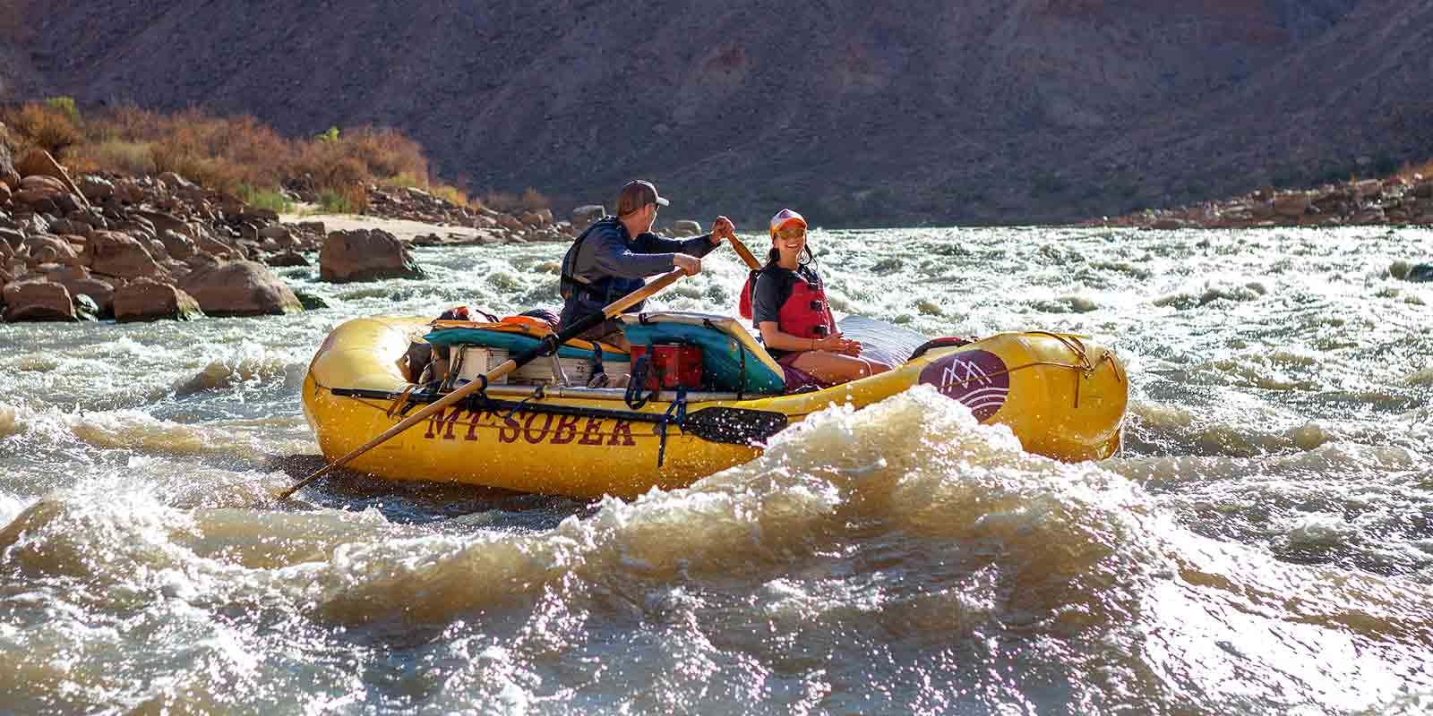 Two people rafting down rapids in a yellow raft.